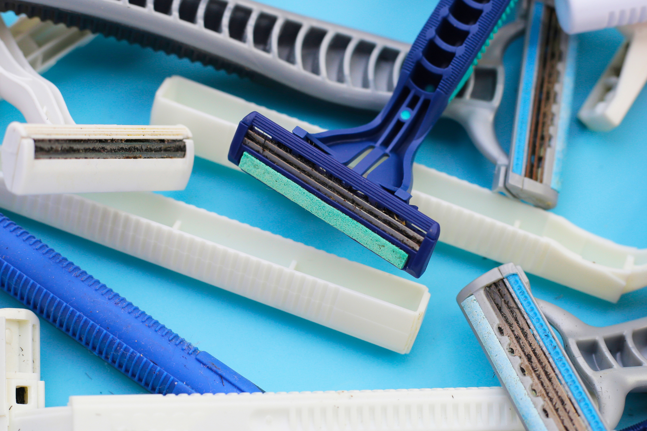 Close-up of various disposable razors and razor blade covers scattered on a light background