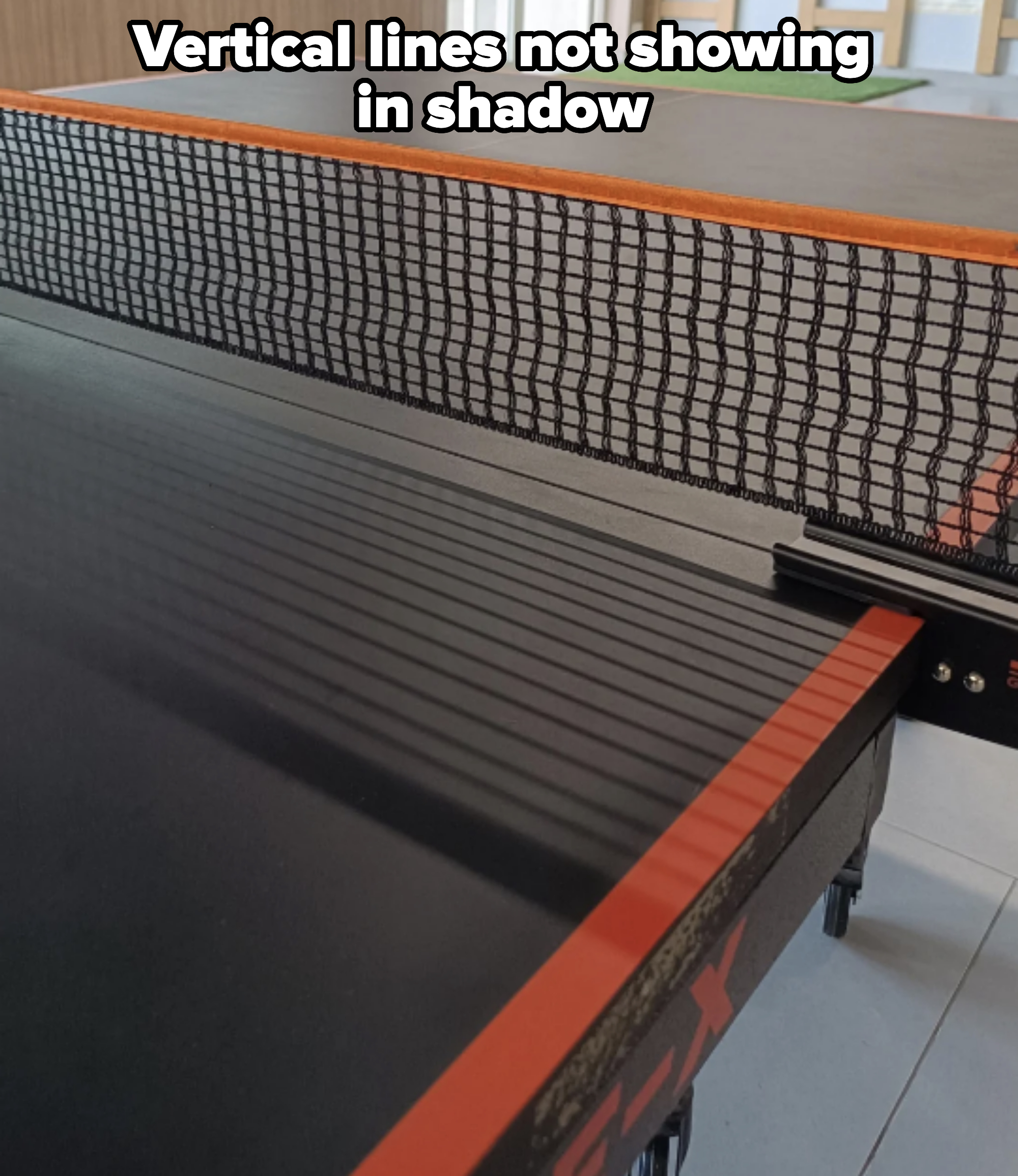 Close-up of a ping pong table with a net secured across the middle, inside a room with a glossy floor and large windows