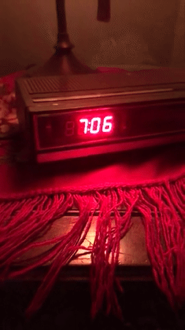 The image shows a digital clock displaying 7:06, placed on a table with a fringed cloth