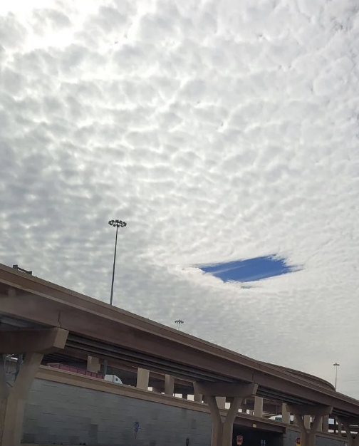 Cloud-covered sky with a small, clear blue patch above an overpass. Streetlights and buildings are visible in the background