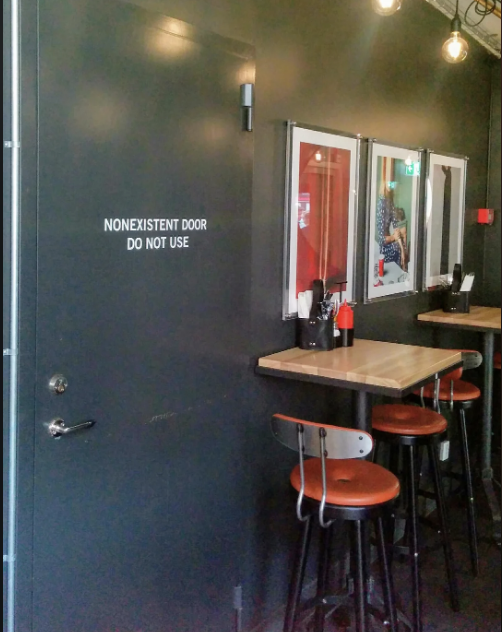 A diner-like setting with a door labeled "NONEXISTENT DOOR DO NOT USE" beside a small dining area with wooden tables and chairs