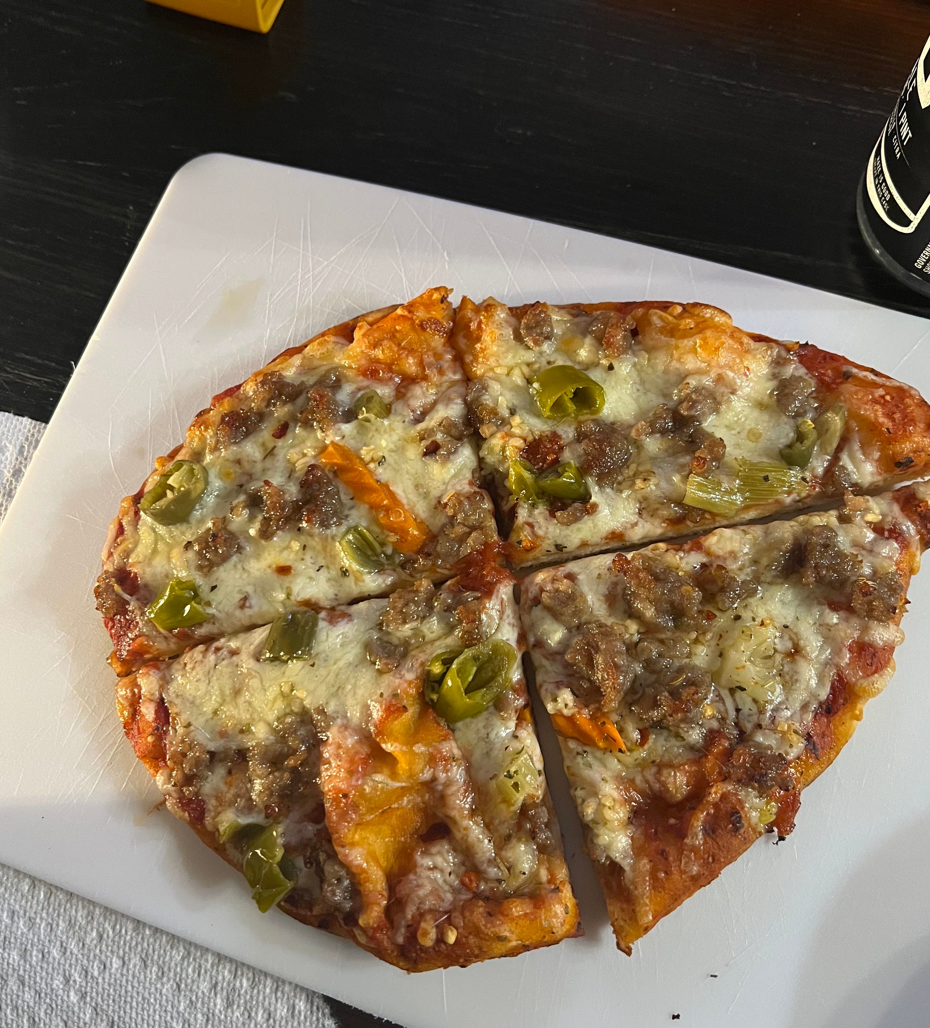 A partially eaten pizza with pepperoni, sausage, and green peppers on a white cutting board next to a small yellow toy truck