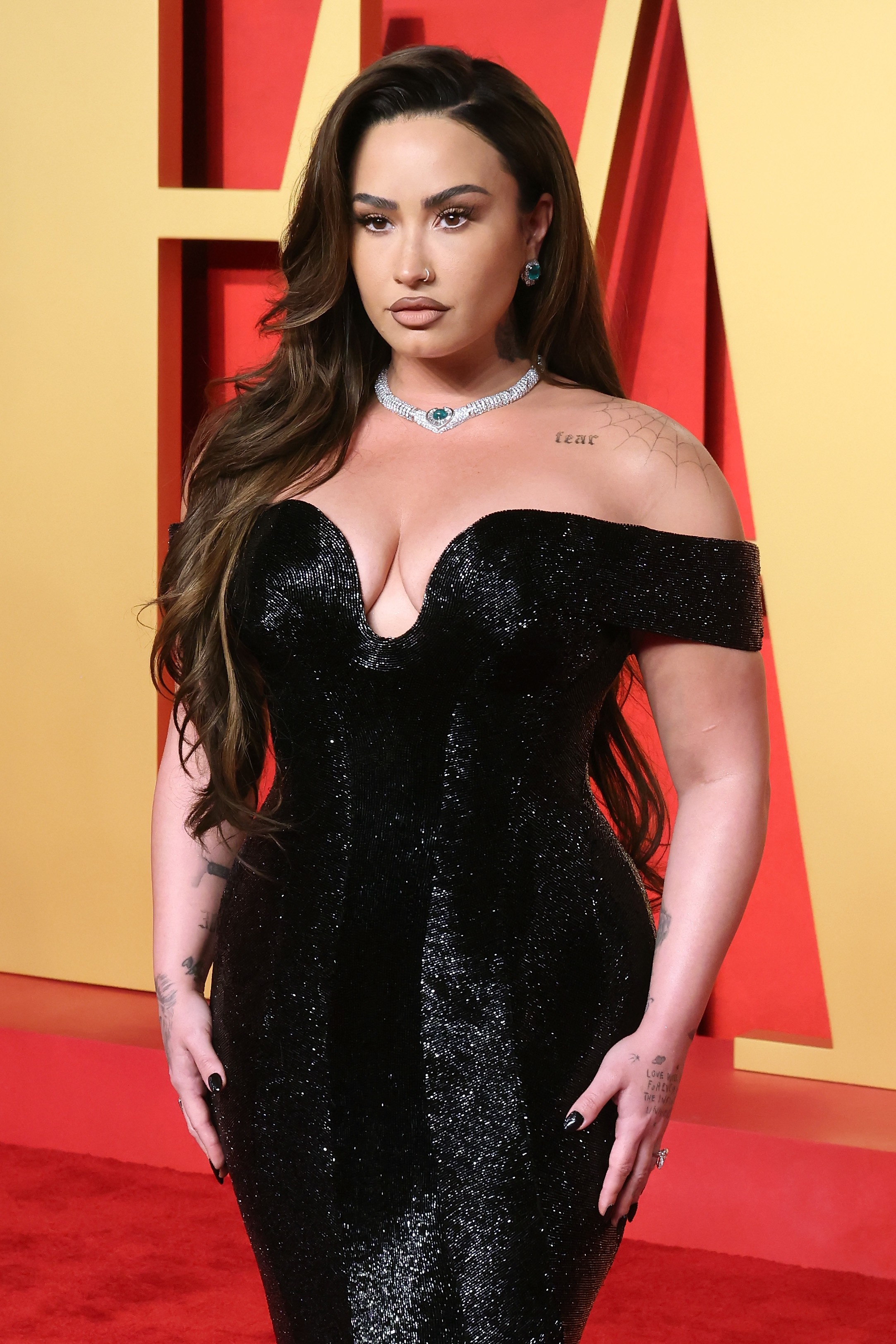 Demi Lovato on the red carpet wearing an elegant, off-shoulder gown with sparkling details and a diamond necklace