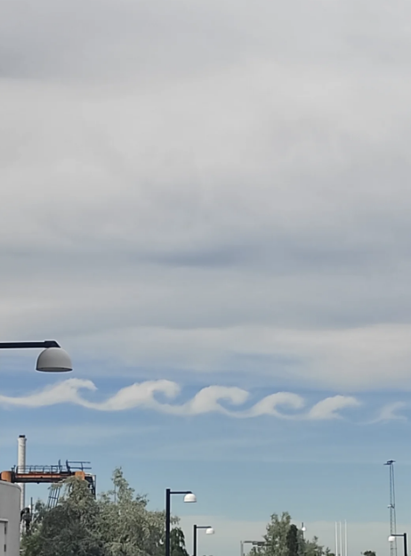 Kelvin-Helmholtz clouds forming wave-like patterns in the sky above a cityscape, with street lights and industrial structures visible below