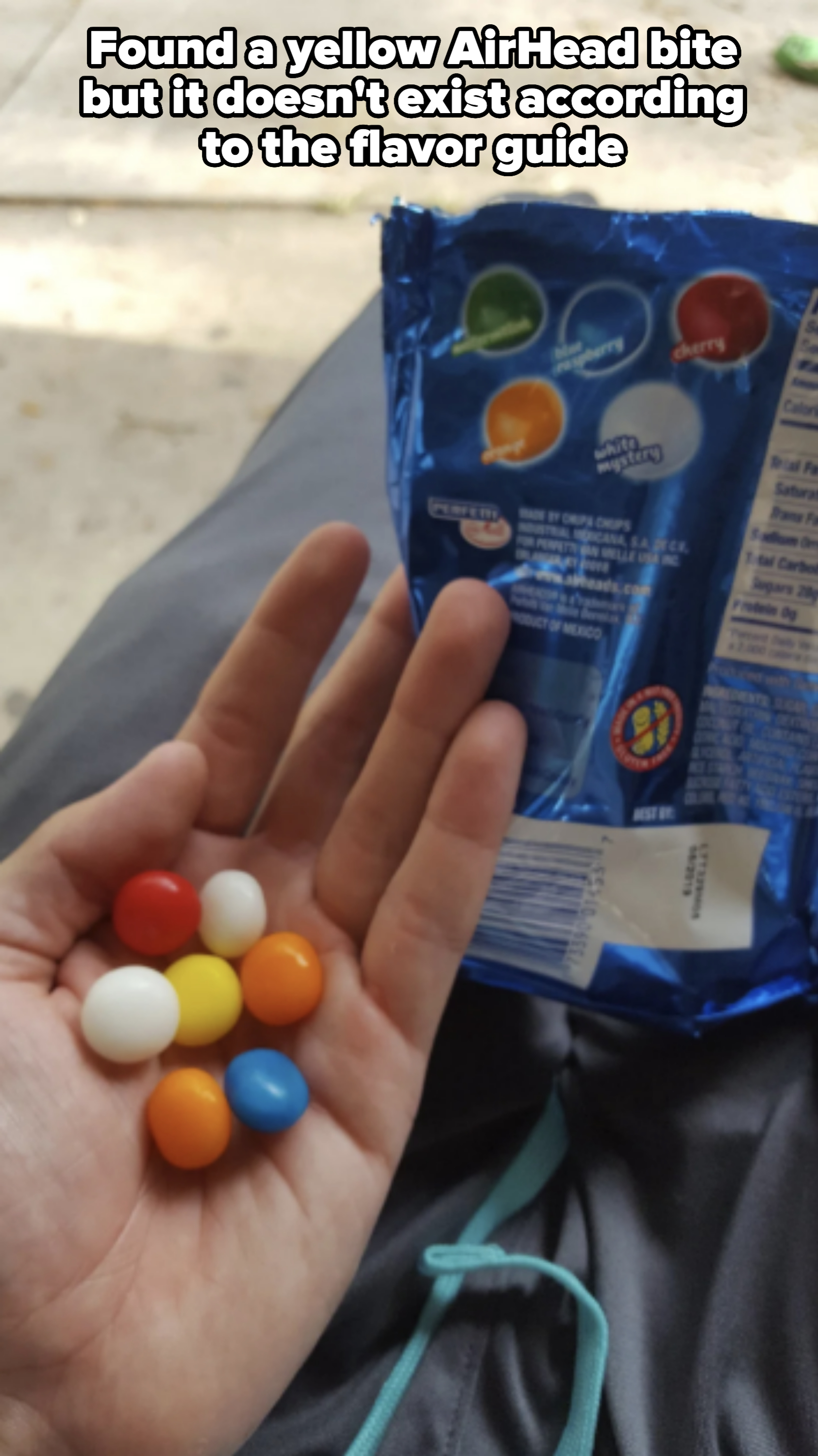 Hand holding various candies with an open blue candy bag showing assorted flavors in the other hand. The bag is partially shown