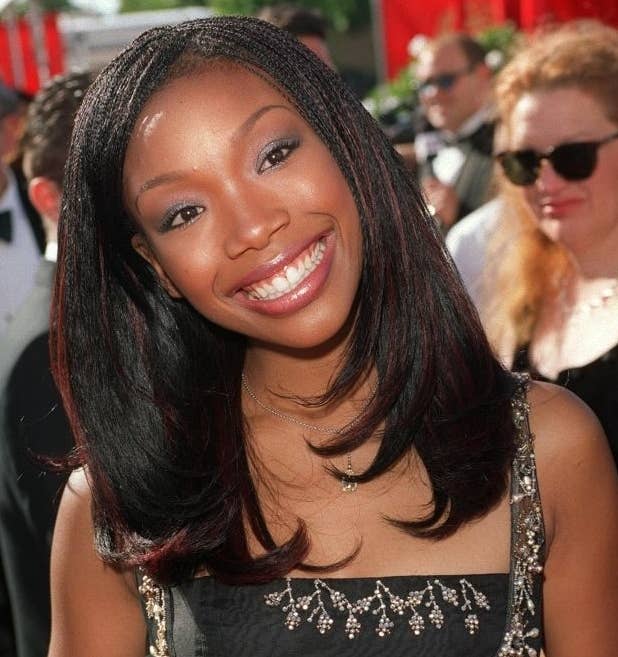Brandy Norwood smiles at the camera while posing on a red carpet in an elegant black dress with intricate detailing