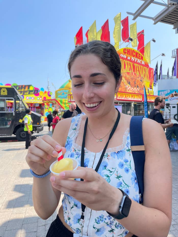 Woman in a festival setting enjoys lemon sorbet on a sunny day. Food trucks and colorful banners in the background highlight a lively food fest atmosphere