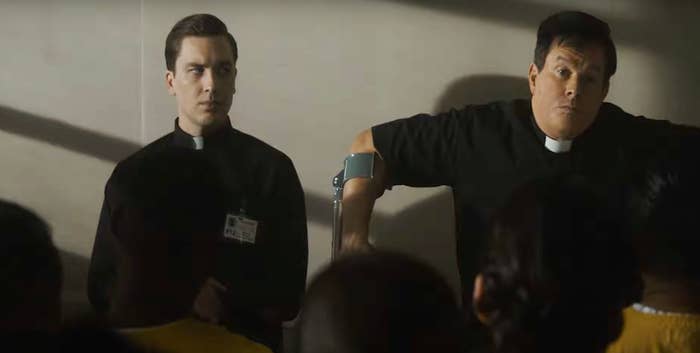 Two men in priest attire stand before an audience. One uses a crutch. They appear serious and focused. Names unknown