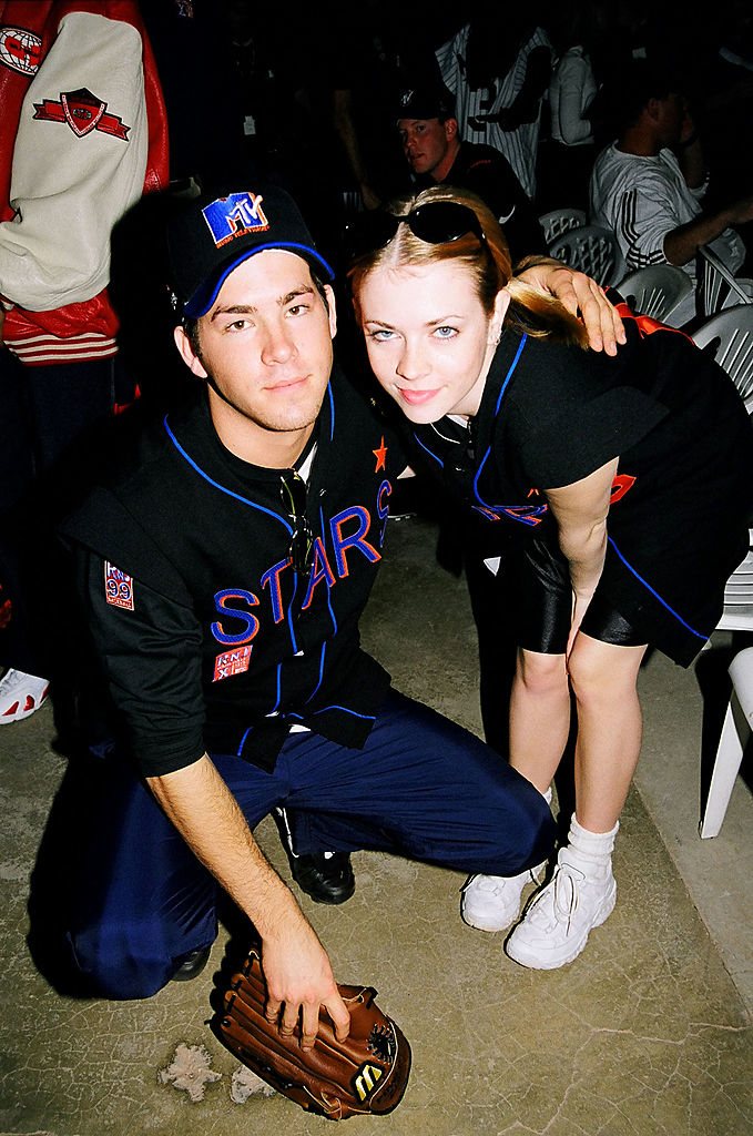 Ryan Reynolds and Melissa Joan Hart are dressed in baseball jerseys, crouching with a baseball glove, at an event