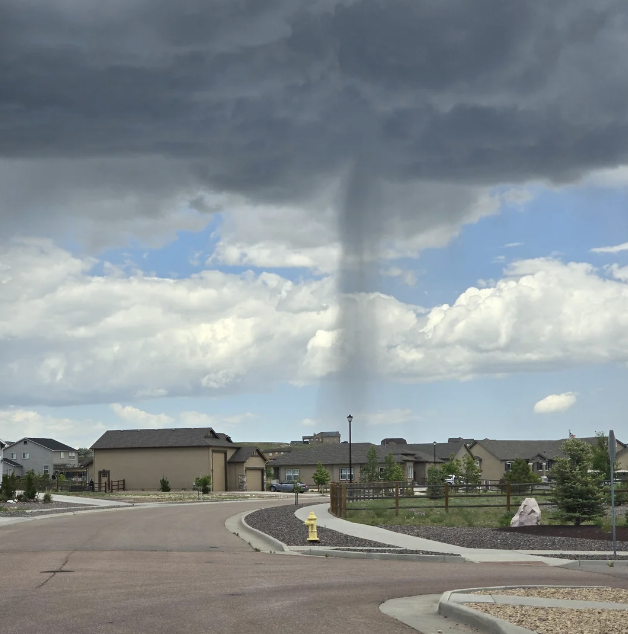 Tornado funnel cloud descending from dark storm clouds over a suburban neighborhood, with homes and streets visible below