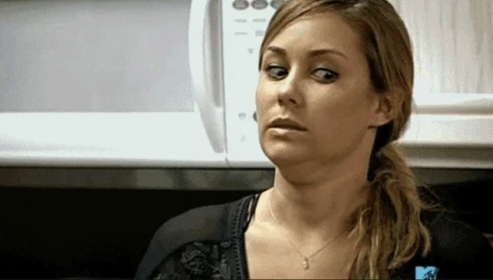 A woman with long hair in a ponytail looks to her right with a concerned expression indoors