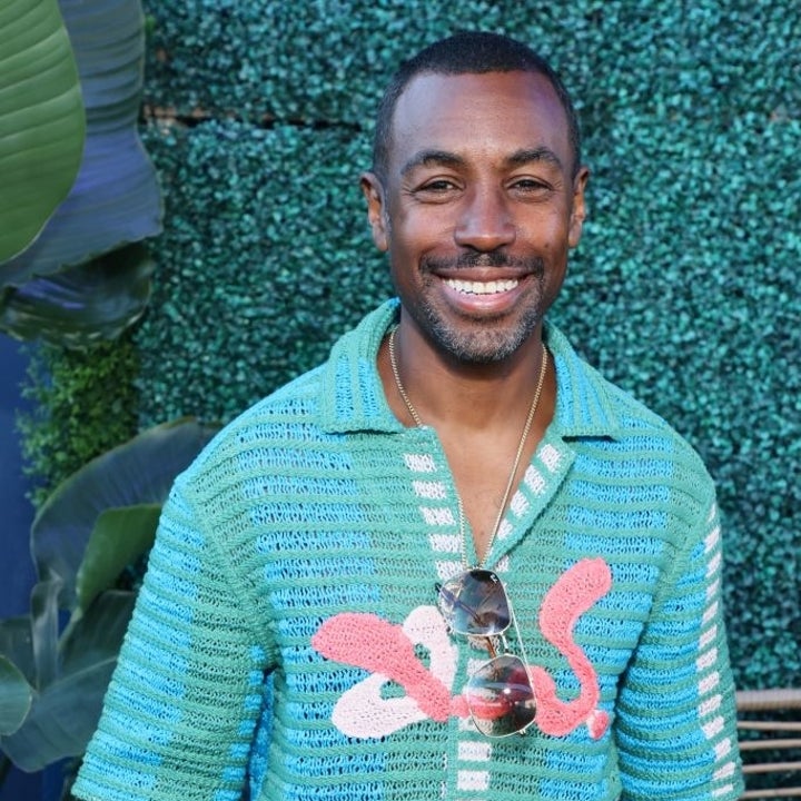 Man smiling in a patterned shirt with sunglasses draped around his neck, standing in front of a leafy background. Name unknown