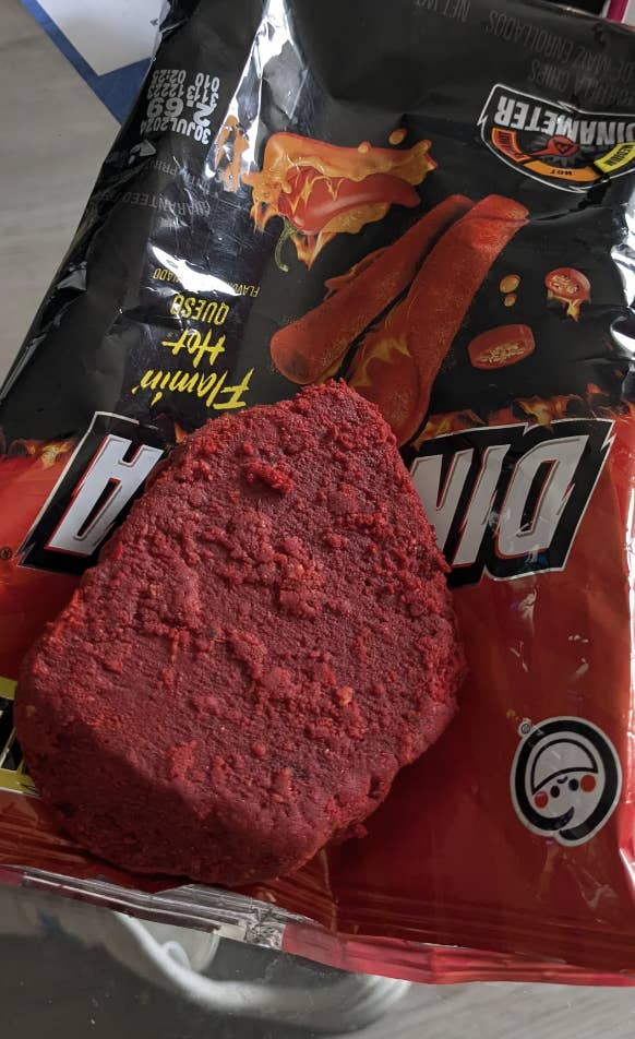 Close-up of an opened bag of Doritos Dinamita chips with one chip, covered in red seasoning, placed on top of the bag