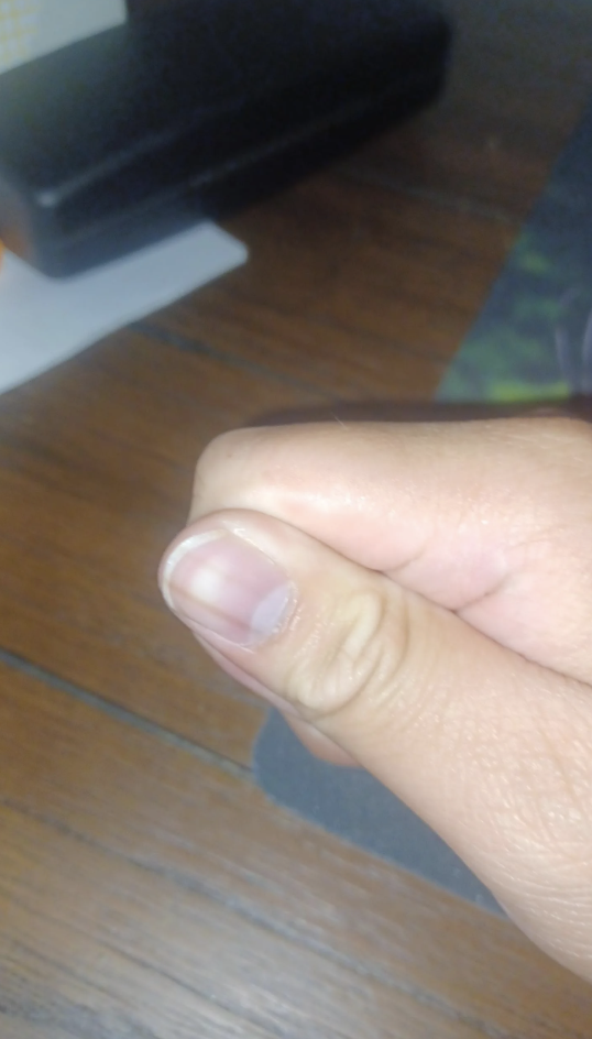 Close-up of a person's hand making a thumbs-up gesture with a small part of a textured wooden surface in the background