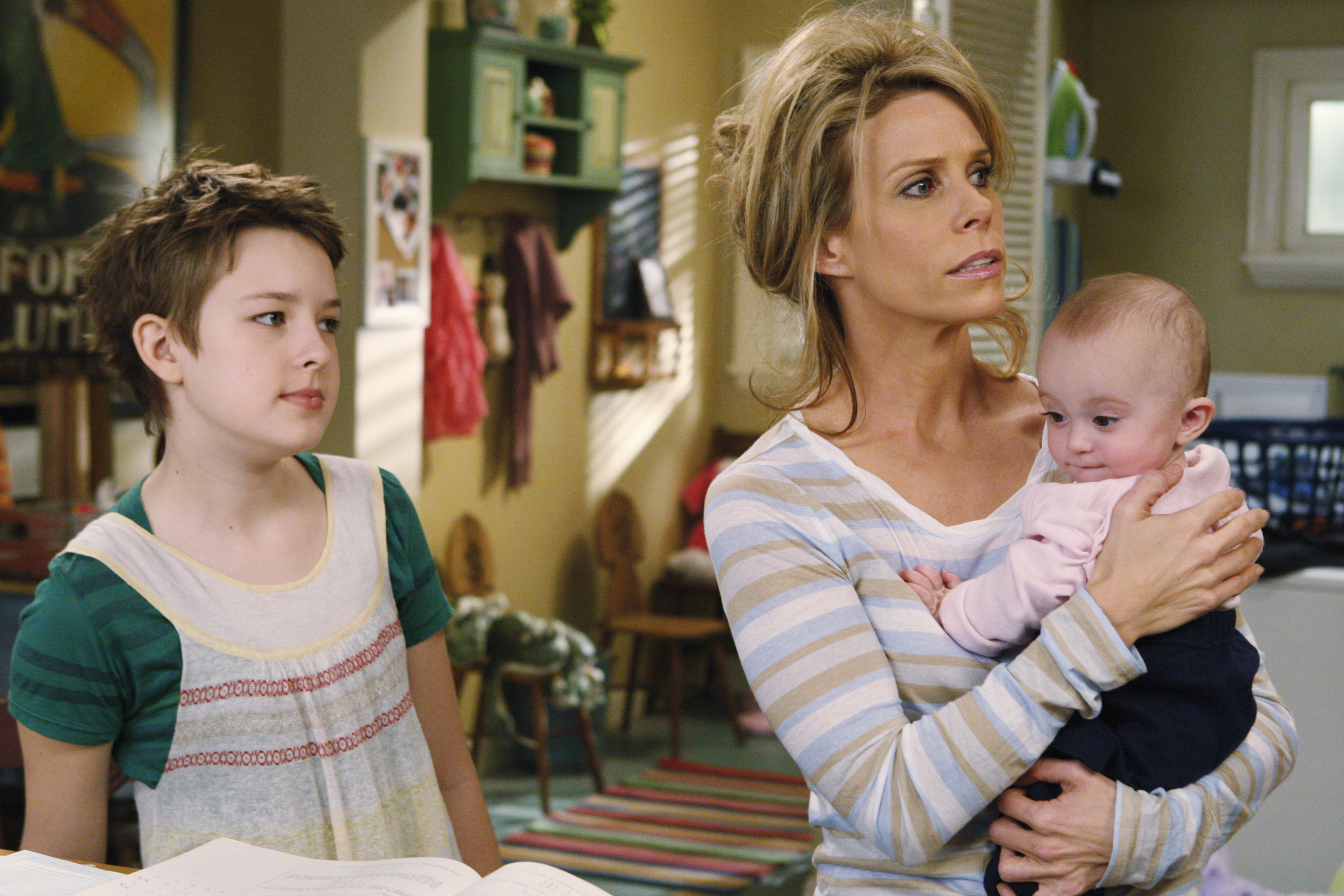 Charlotte Foley, Cheryl Hines, and a baby standing in a kitchen/laundry room setting in a scene from "In the Motherhood"