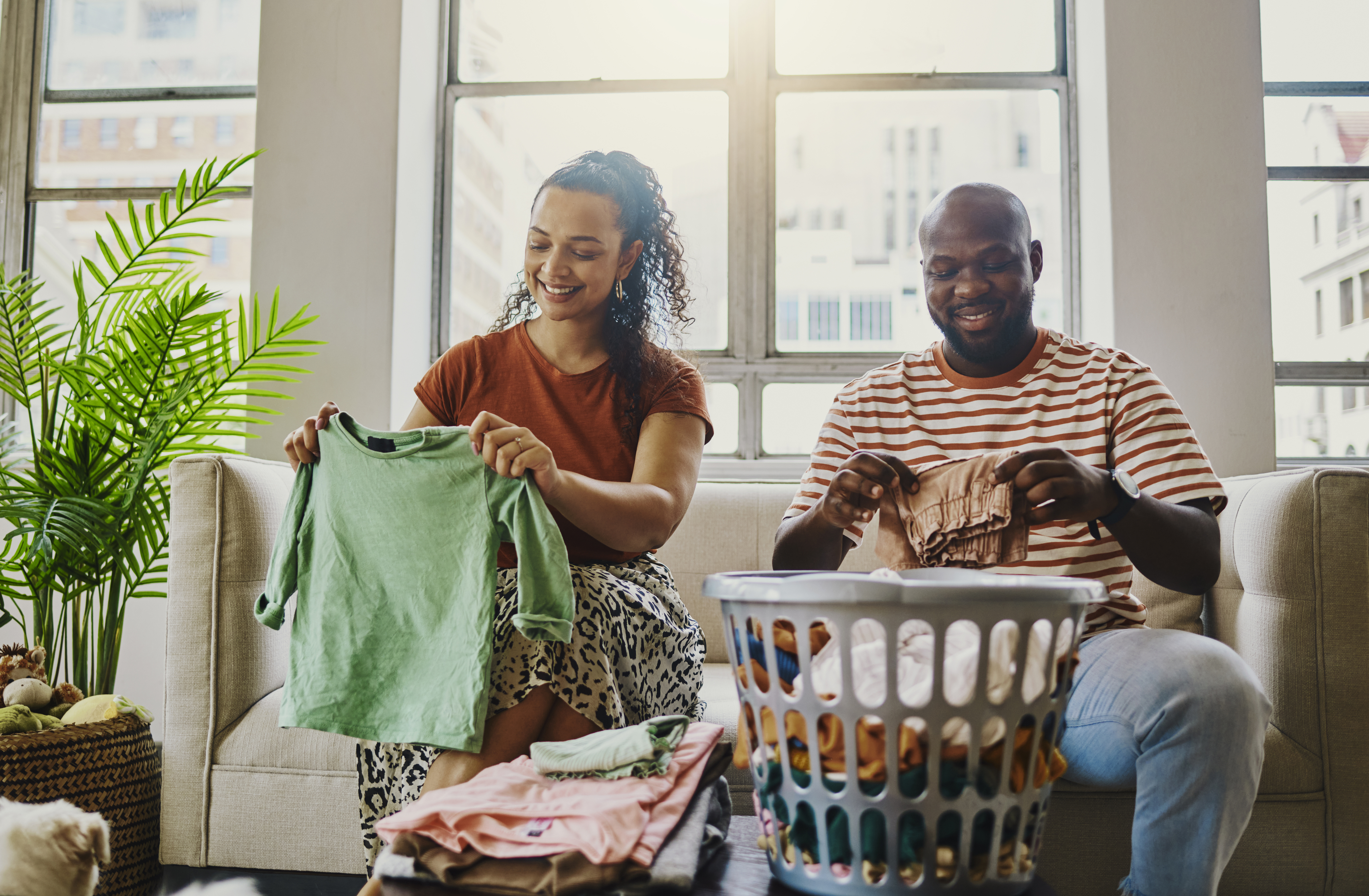 A woman and a man sit on a couch folding laundry