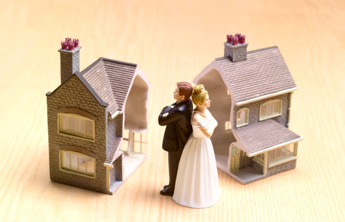 A bride and groom figurine stand back-to-back between two split model houses, symbolizing divorce or separation