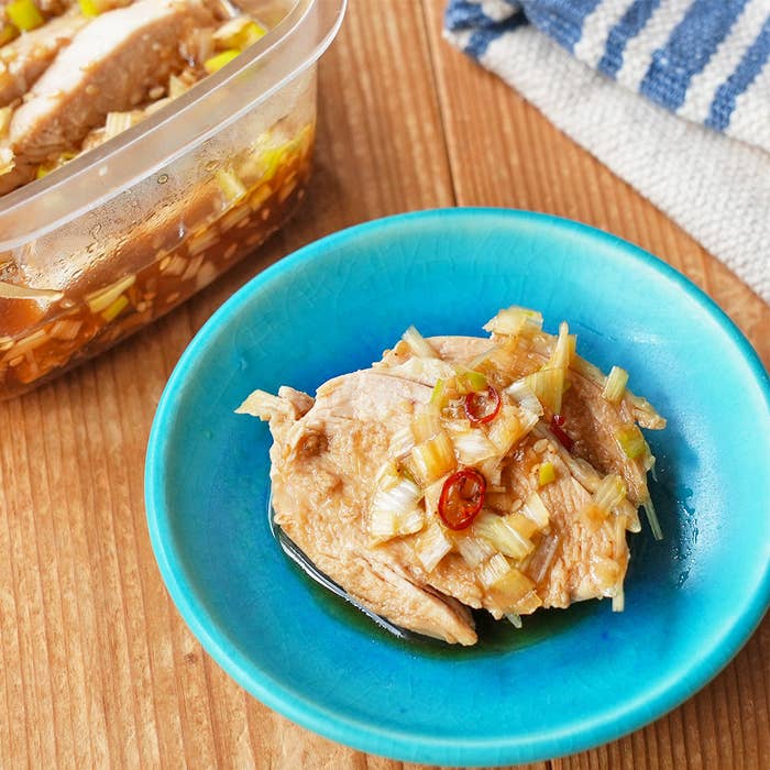 青い皿に盛られた鶏肉とネギ、唐辛子の料理。背景にストライプの布とプラスチックの容器が見える。