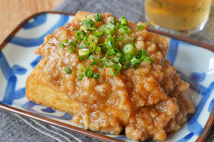 お皿に盛られた麻婆豆腐に似た料理。刻んだネギが上に載っている。バックグラウンドに冷たい飲み物がある。
