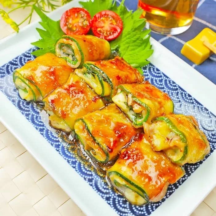 皿の上に盛られた焼きズッキーニロールの料理。葉とトマトのスライスが添えられています。