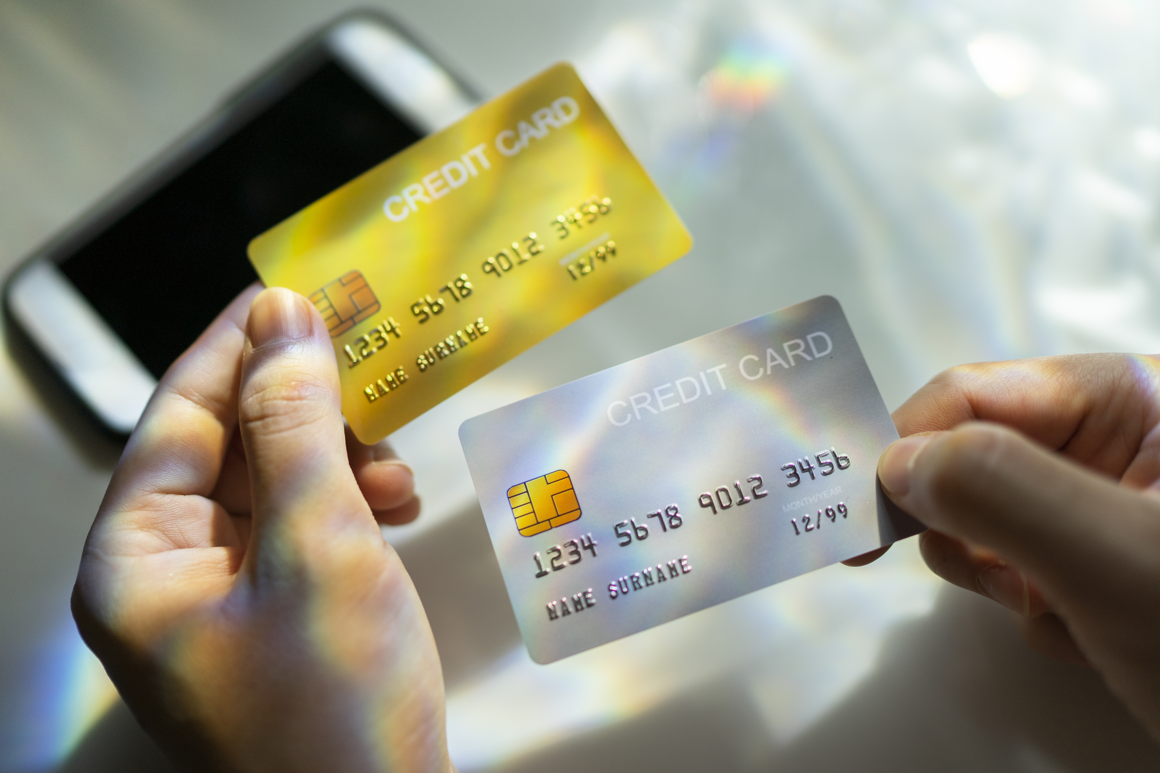 Hands holding two credit cards, one gold and one silver, above a smartphone