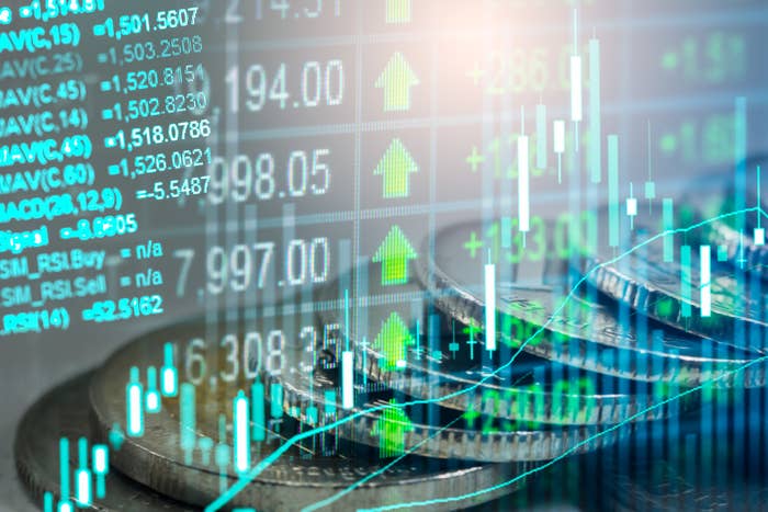 Stock market screen displaying financial data and rising trends superimposed over a stack of coins