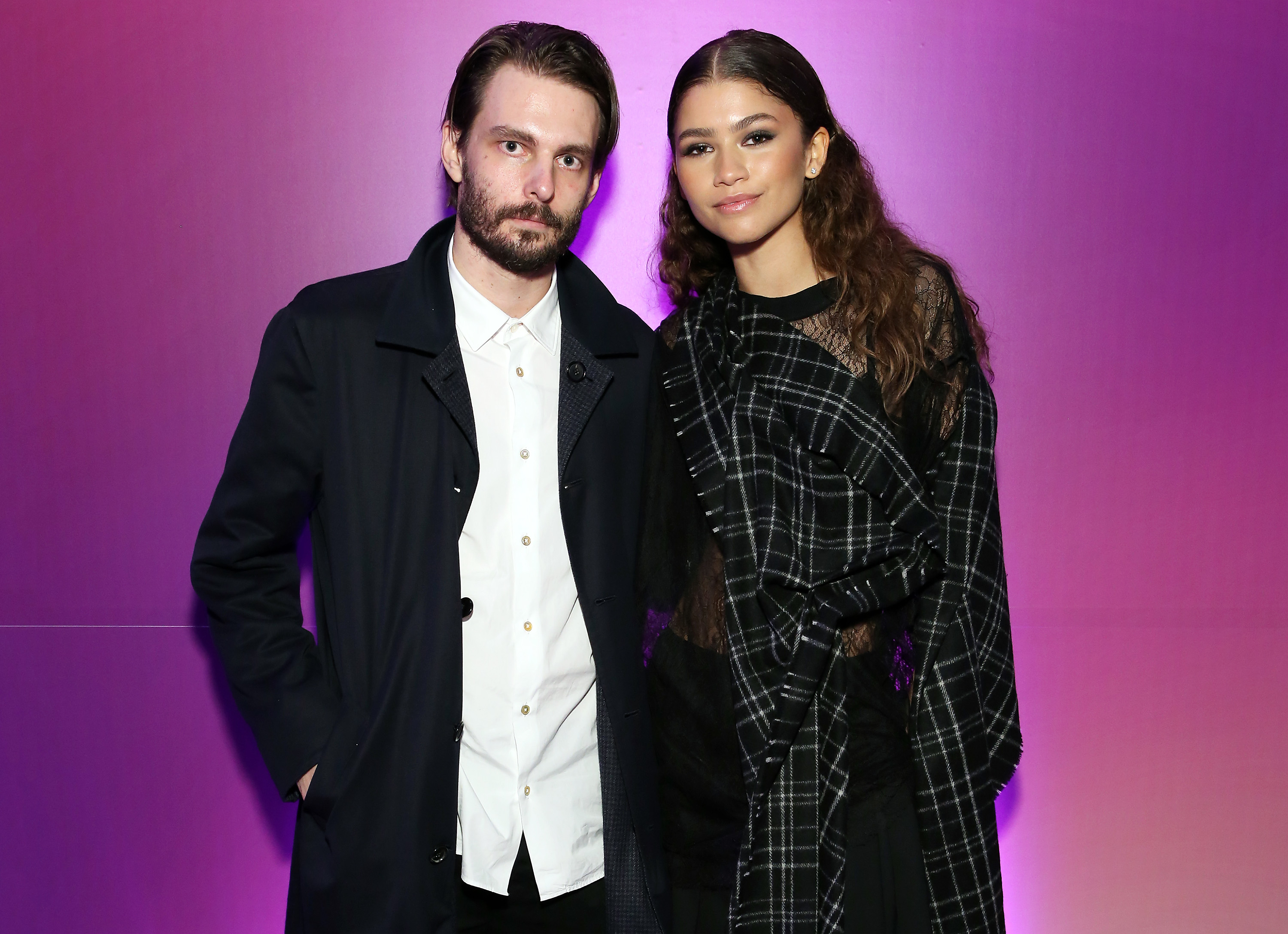 Zendaya and Sam Levinson stand together in stylish black and white outfits against a plain backdrop