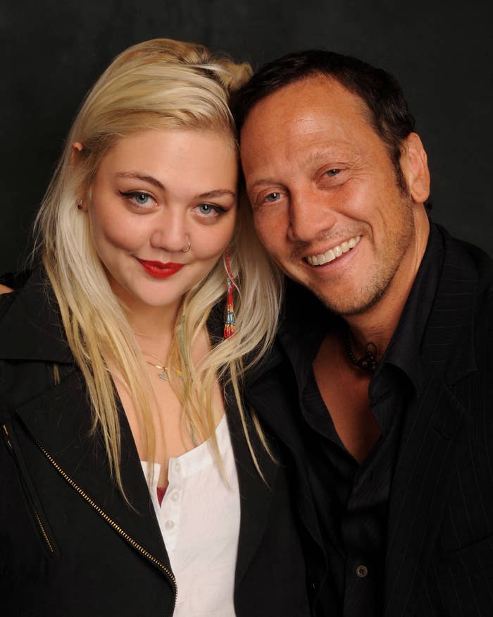 Elle King and Rob Schneider smiling, with Rob Schneider wearing a dark suit and Elle King in a casual top with a dark jacket
