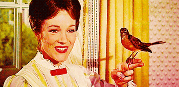 Julie Andrews, dressed in a Victorian-style blouse, smiles while holding a robin perched on her finger in a scene from the movie Mary Poppins