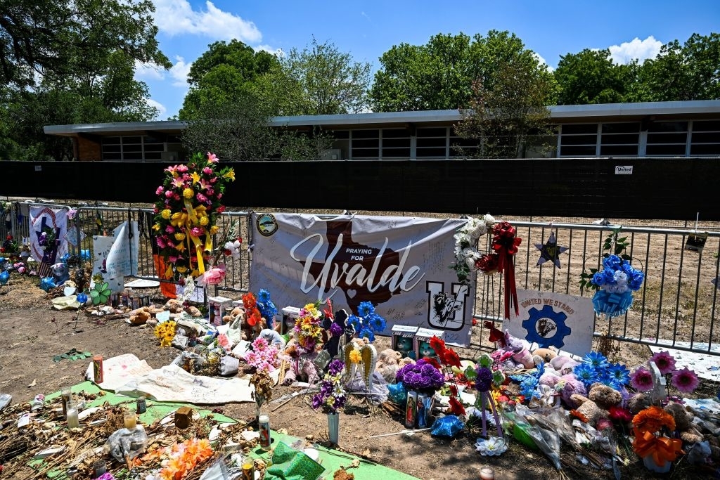 Memorial with flowers, stuffed animals, and banners outside a building in Uvalde, honoring victims of a tragic event