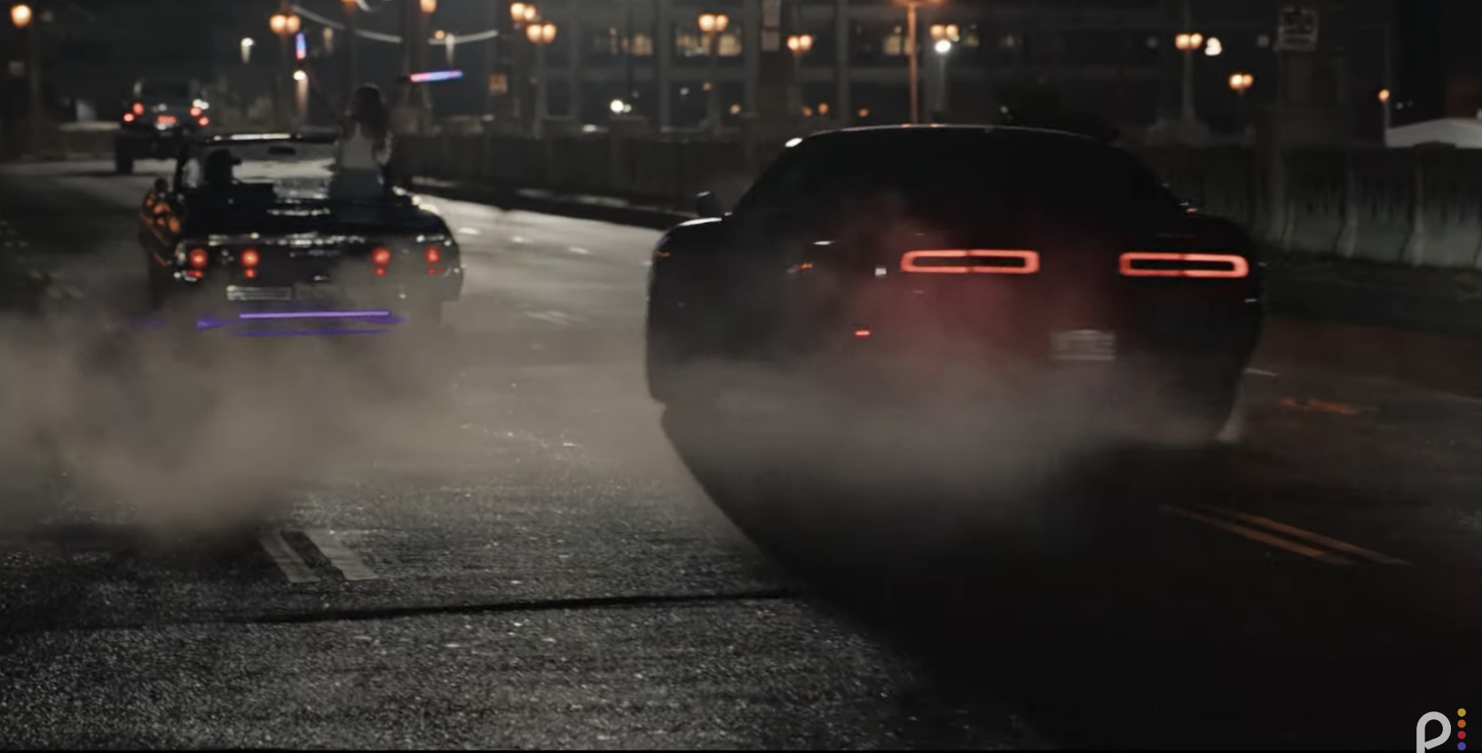 Two cars, one vintage with passengers and one modern, seen drifting on a city street at night amidst smoke clouds