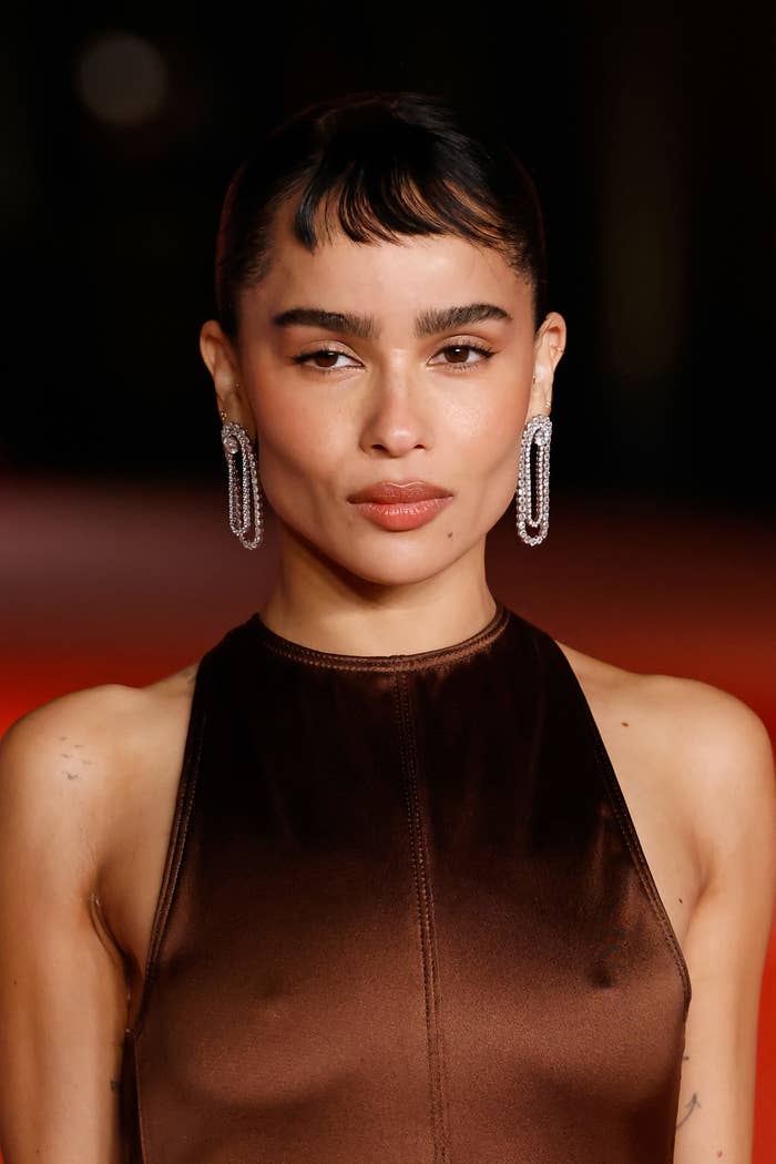 Zoë Kravitz on the red carpet, wearing a sleek, sleeveless dress and statement earrings