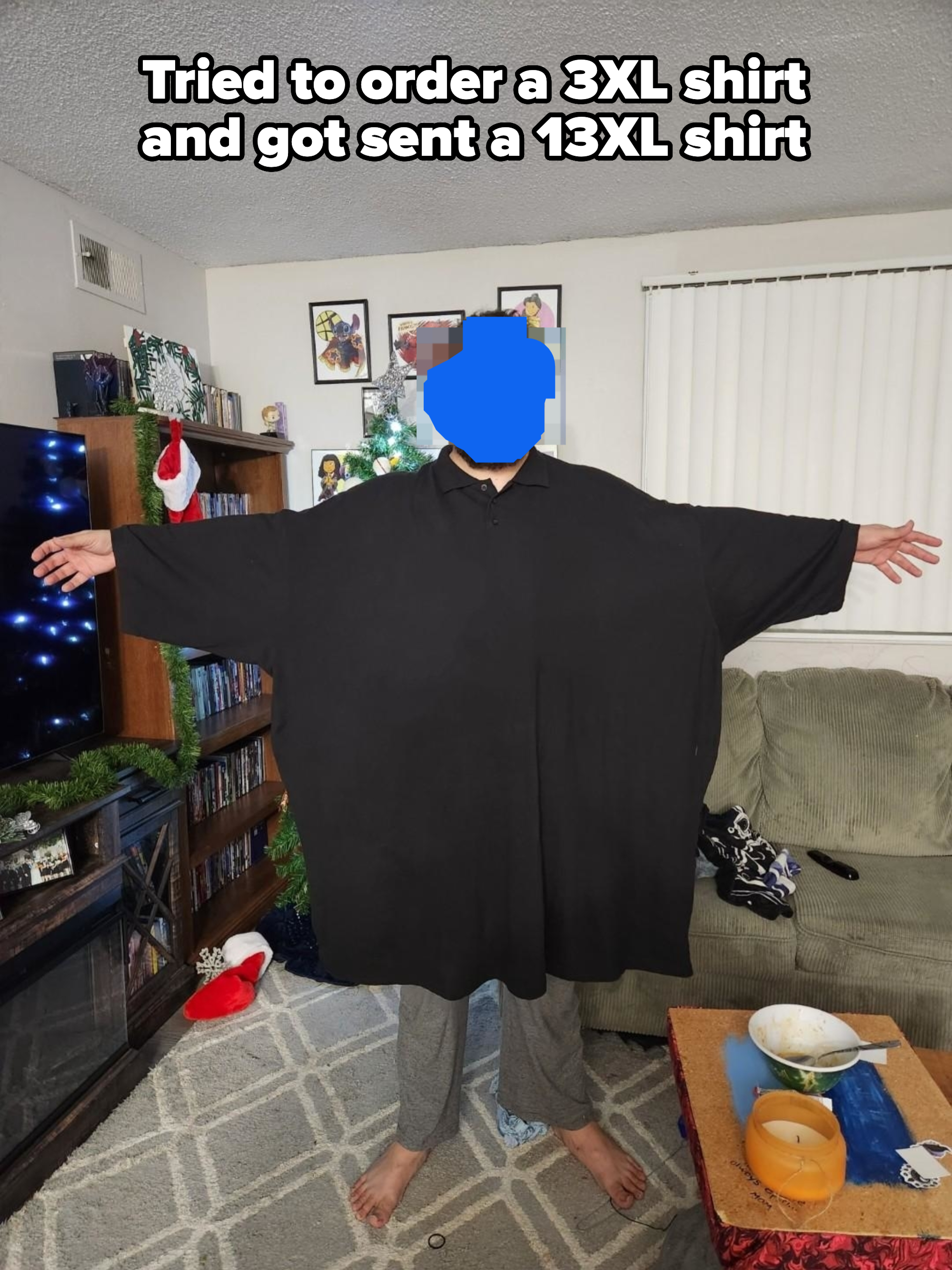 Man standing in a living room with arms outstretched, wearing a very large black shirt that extends past his fingertips