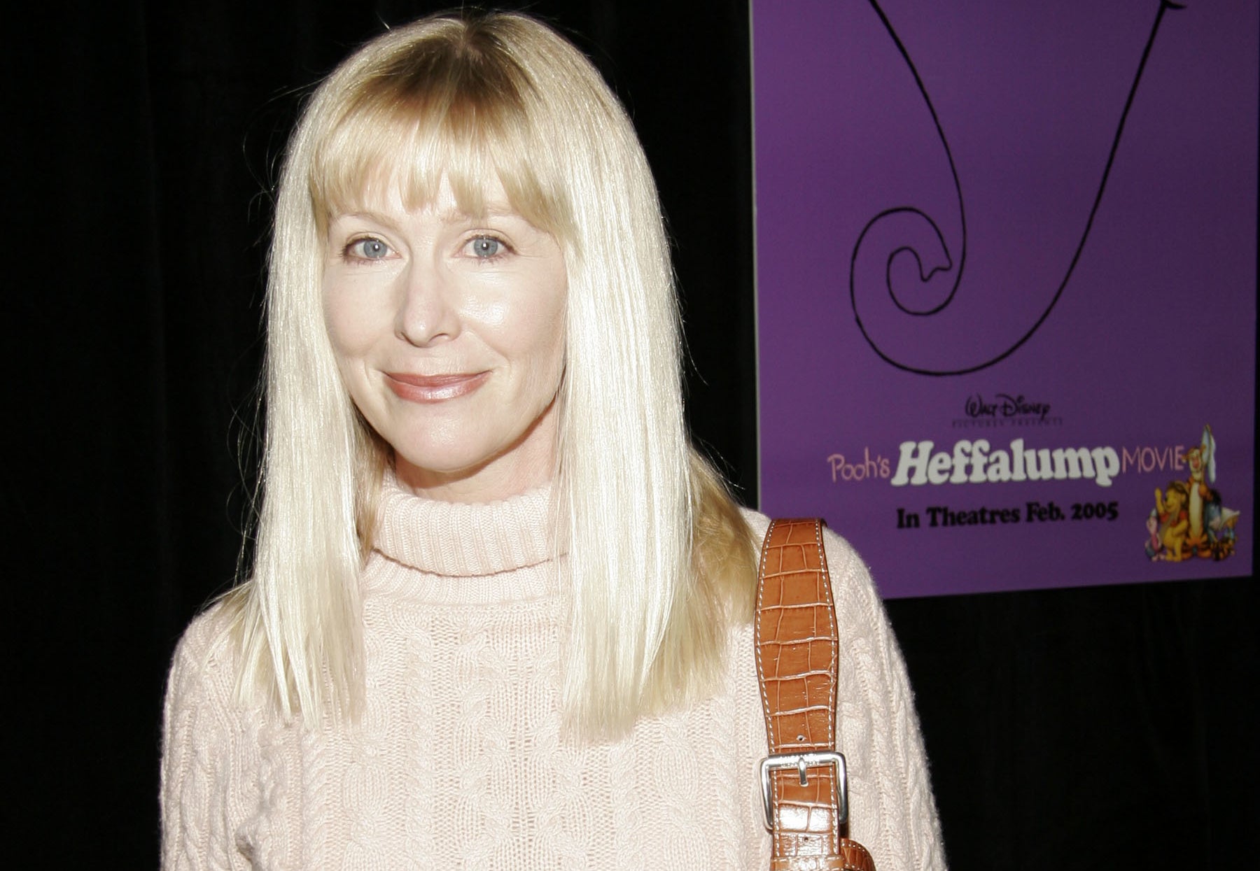 Kath Soucie wearing a cable-knit turtleneck sweater and belted slacks at the premiere of Disney's "Pooh's Heffalump Movie" in front of a promotional poster