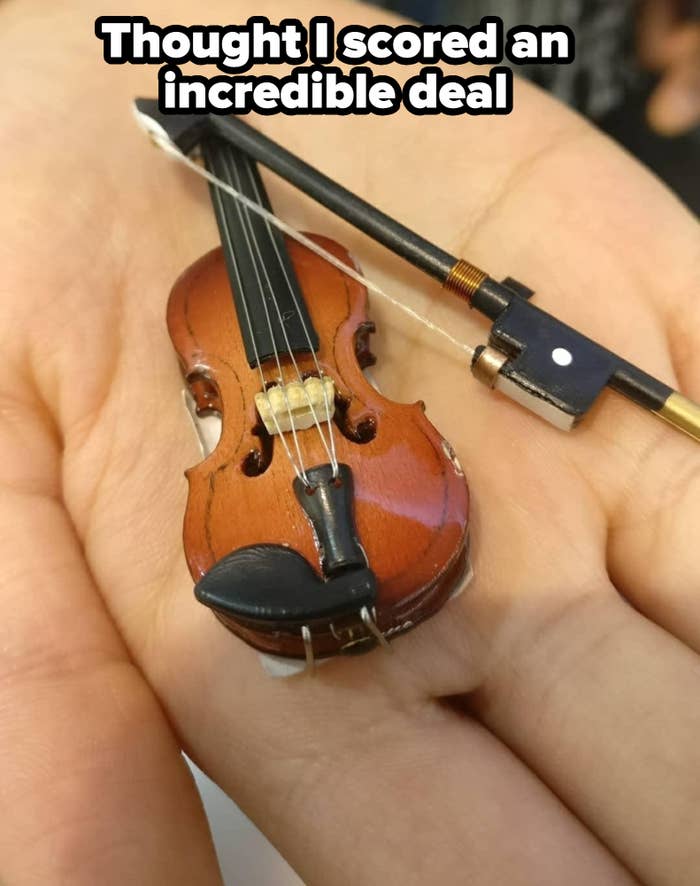 A hand holding a tiny, realistic model of a violin with a bow