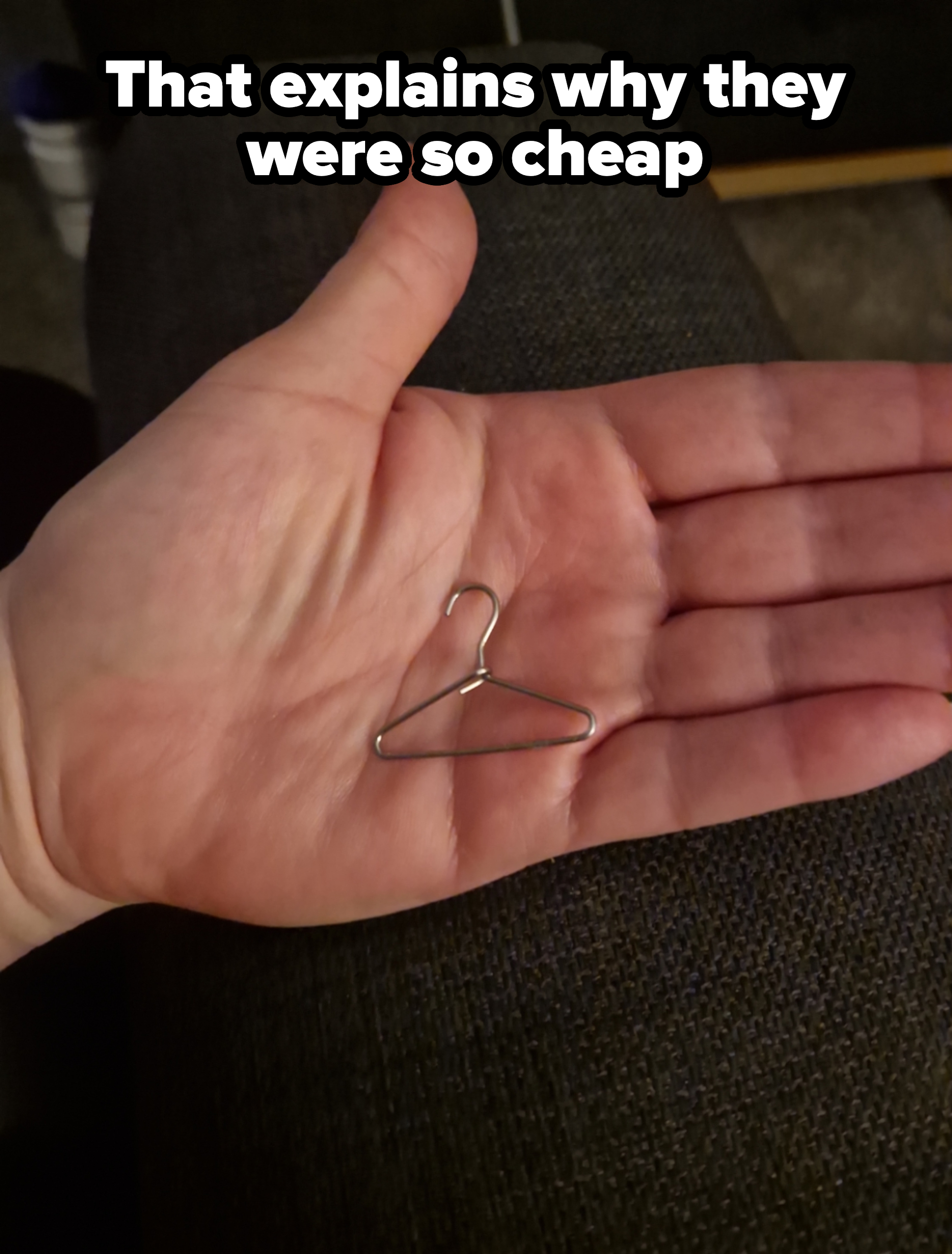 A hand holds a tiny wire hanger placed on its palm for size comparison