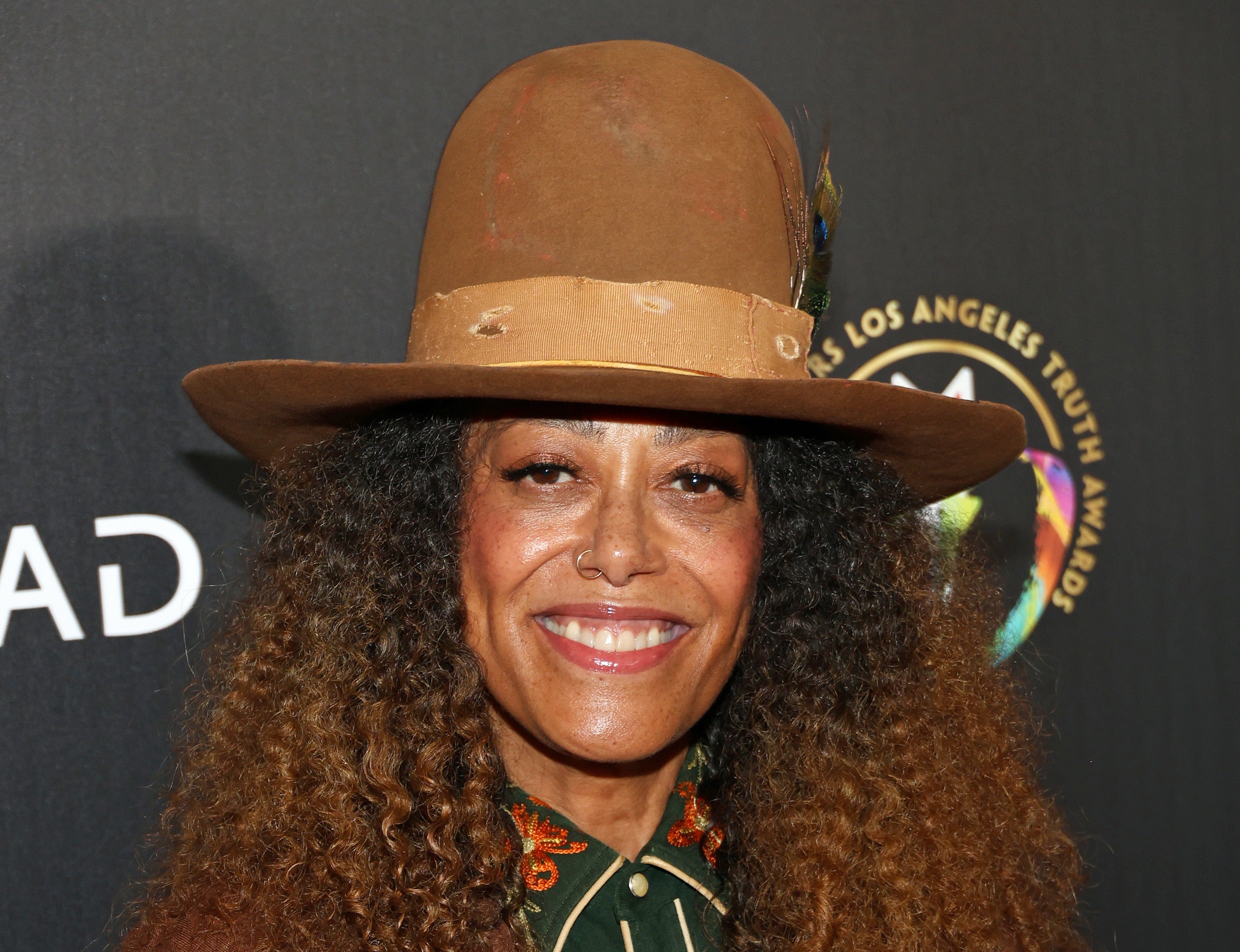 Person smiling, wearing a wide-brimmed hat, a buttoned shirt with detailed embroidery, and a suit jacket at an event. Name of the person is unknown