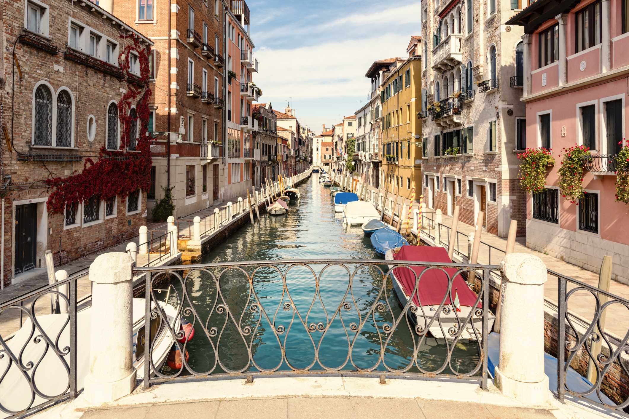 A picturesque canal in Venice, Italy with boats moored along the sides, viewed from a decorative bridge