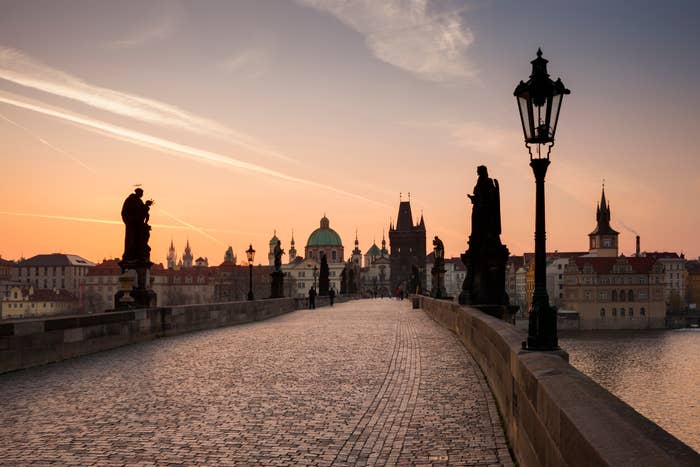 View of Charles Bridge in Prague at sunrise, with silhouettes of statues lining the bridge and historical buildings in the background