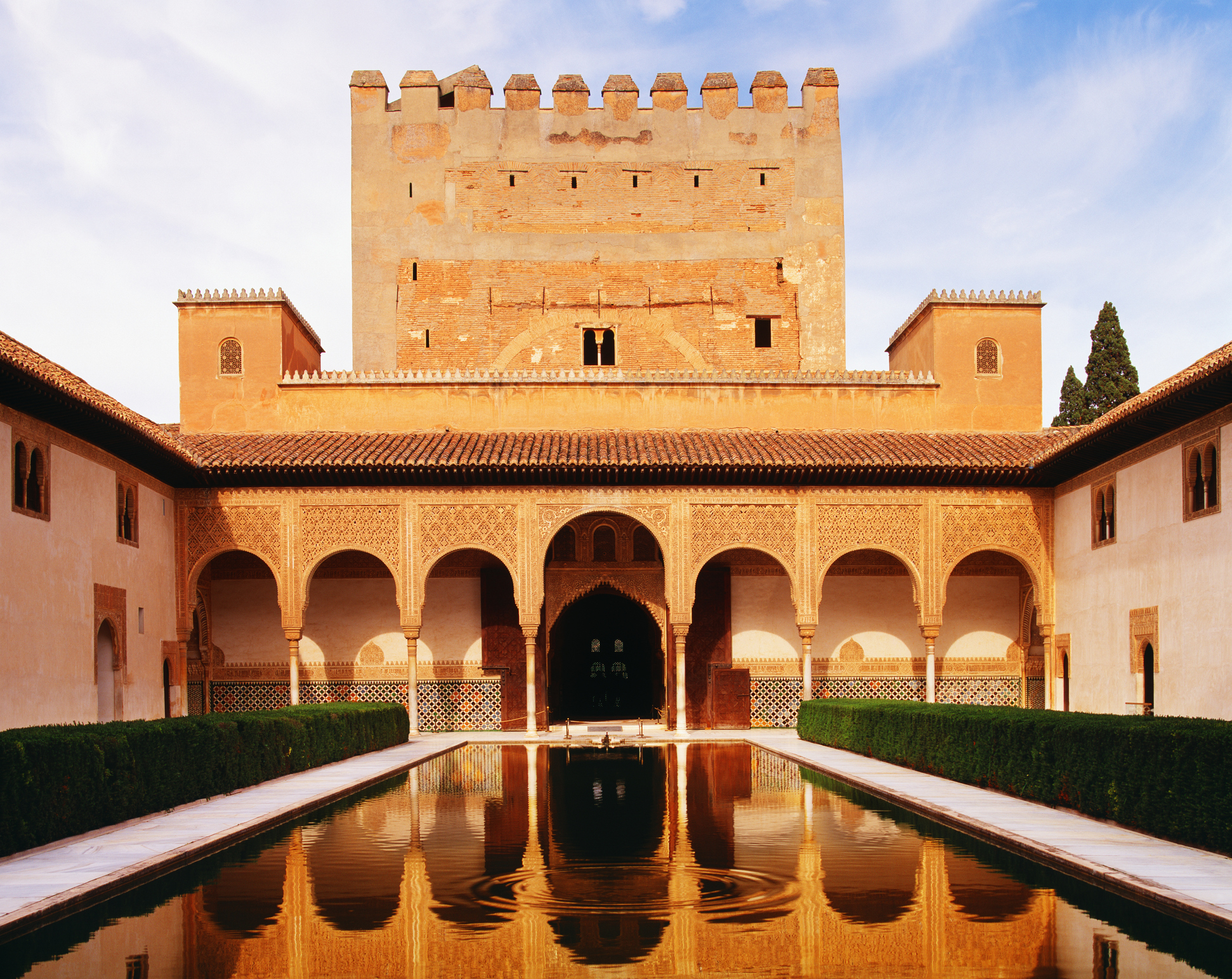 A historic palace with a serene reflecting pool in the foreground, surrounded by archways and a tower. The scene exudes a sense of timeless architecture