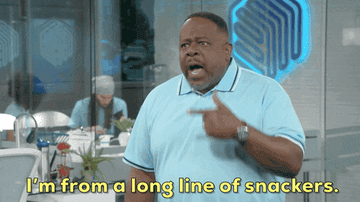 Cedric the Entertainer in a light polo shirt says, "I'm from a long line of snackers." People are seen working in the background