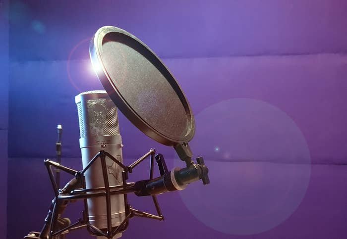 Close-up of a professional microphone and pop filter in a recording studio against a purple background