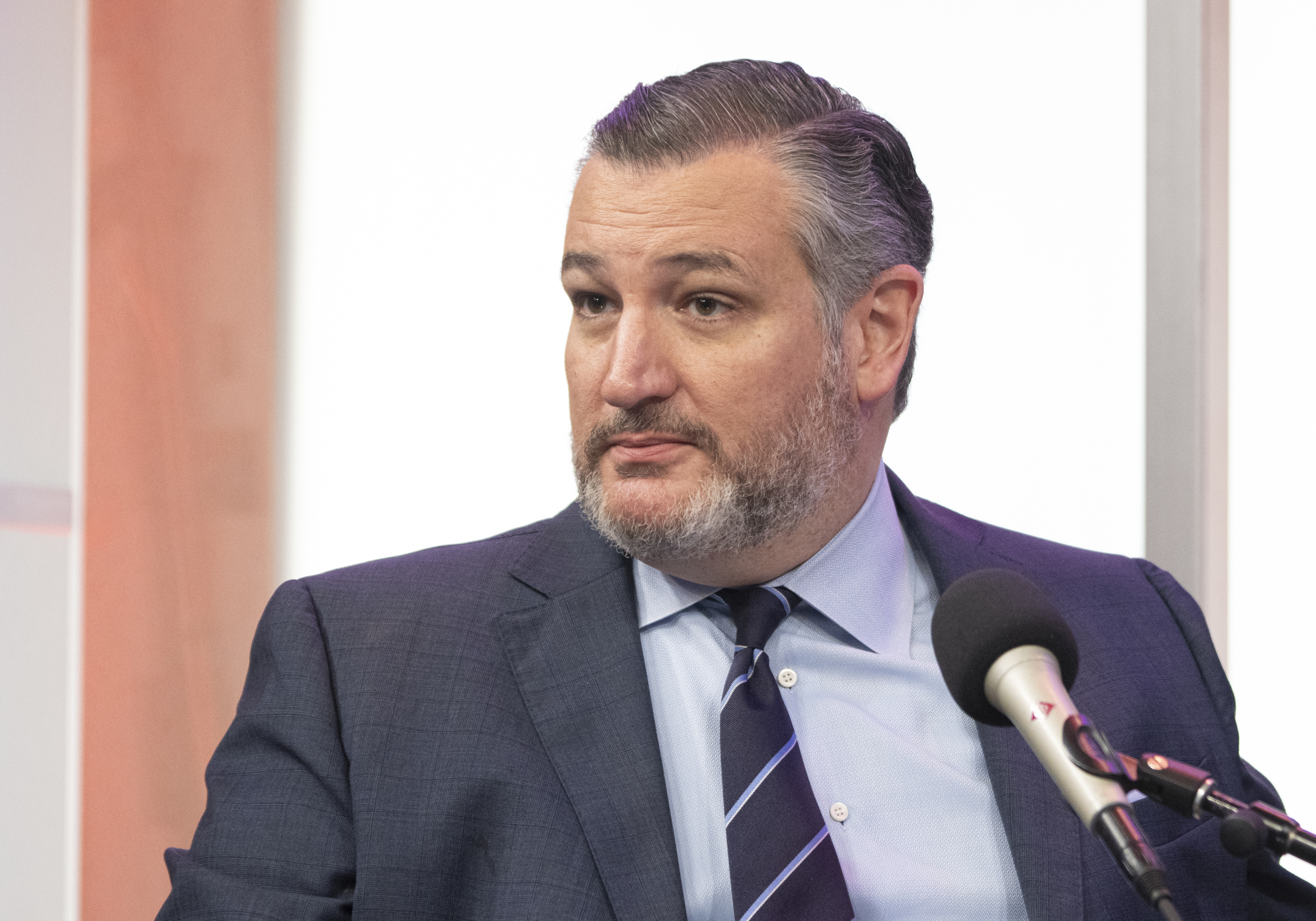 Ted Cruz speaking into a microphone, wearing a suit and a striped tie