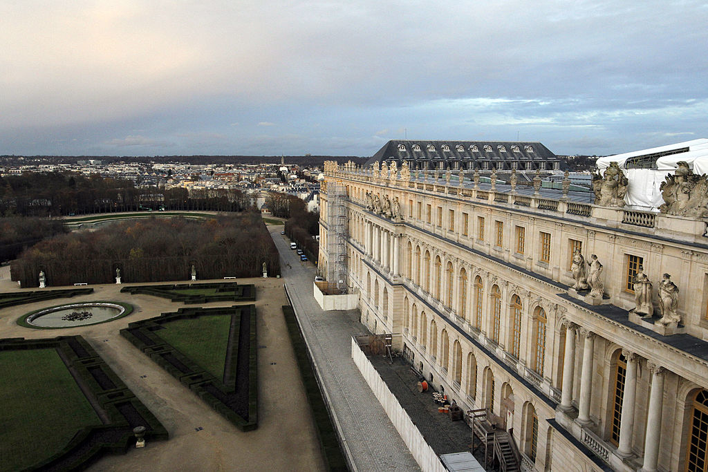 Aerial view of the Palace of Versailles and its formal gardens, with the sprawling landscape of the city visible in the background