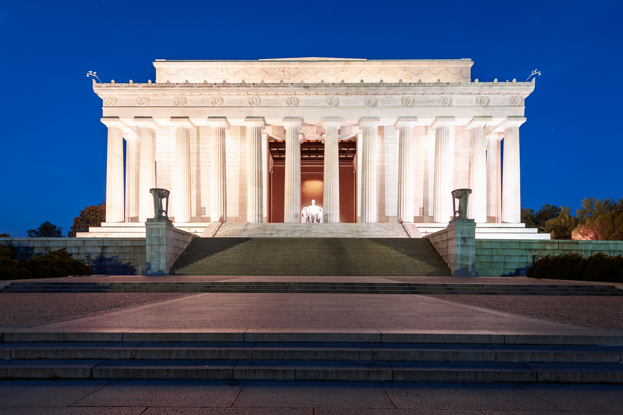 The image shows the Lincoln Memorial at night, with the illuminated statue of Abraham Lincoln visible inside the monument's columns