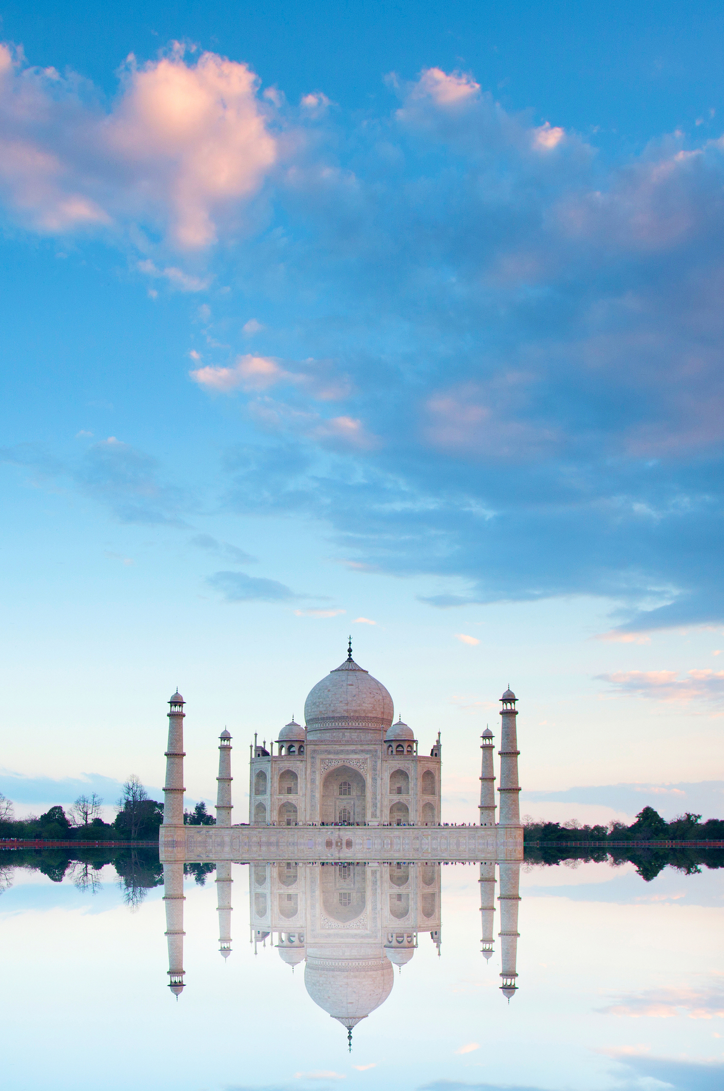 The image shows the Taj Mahal with its reflection in a serene body of water under a sky with scattered clouds