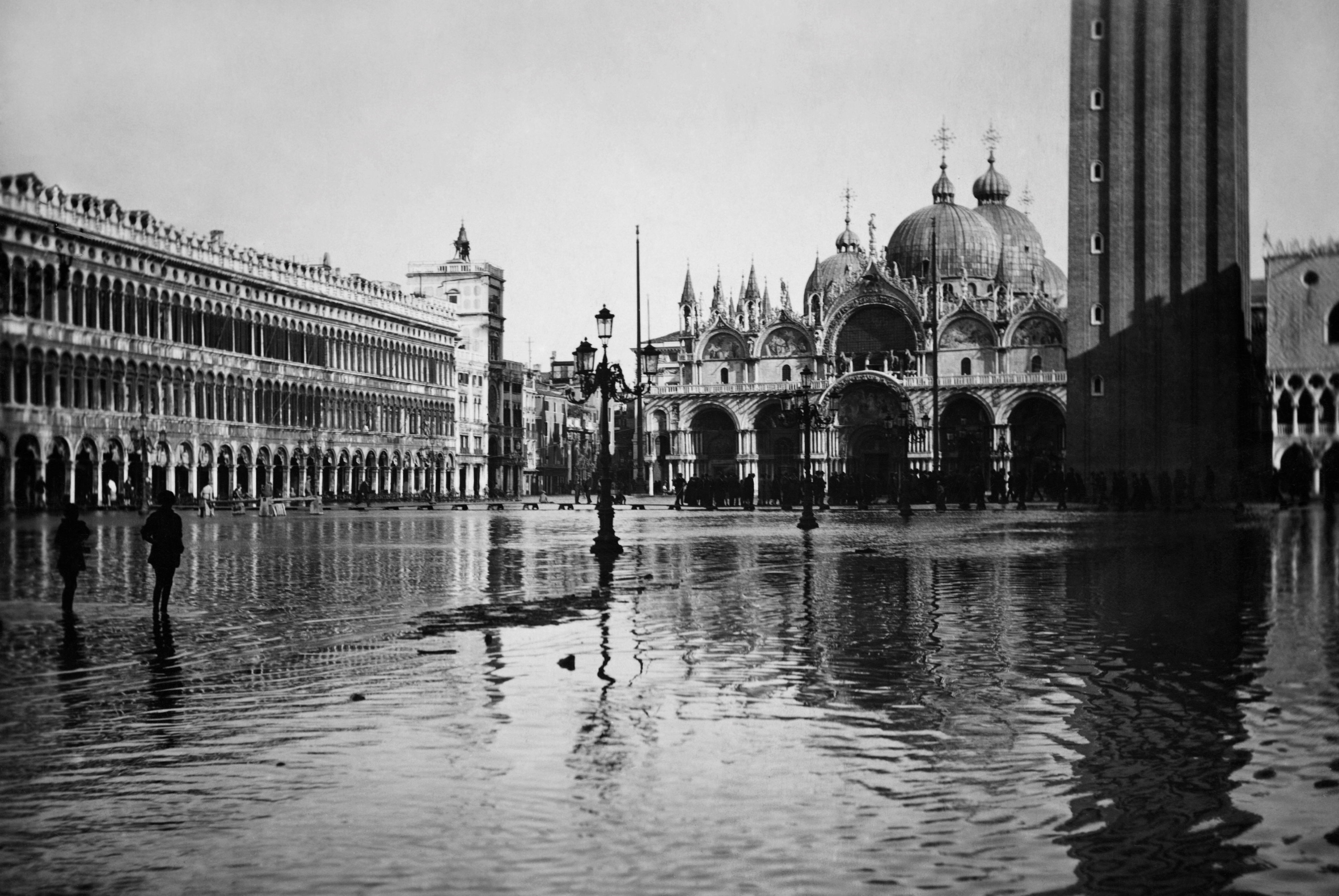Flooded St. Mark's Square (Piazza San Marco) in Venice, with buildings reflected in the water. The domes of St. Mark's Basilica and the Campanile tower are visible