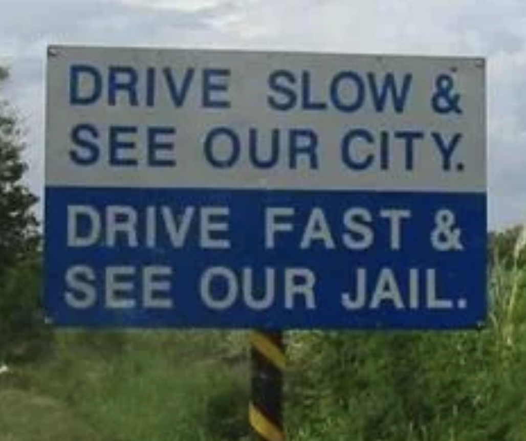 A roadside sign reads, "Drive slow & see our city. Drive fast & see our jail."