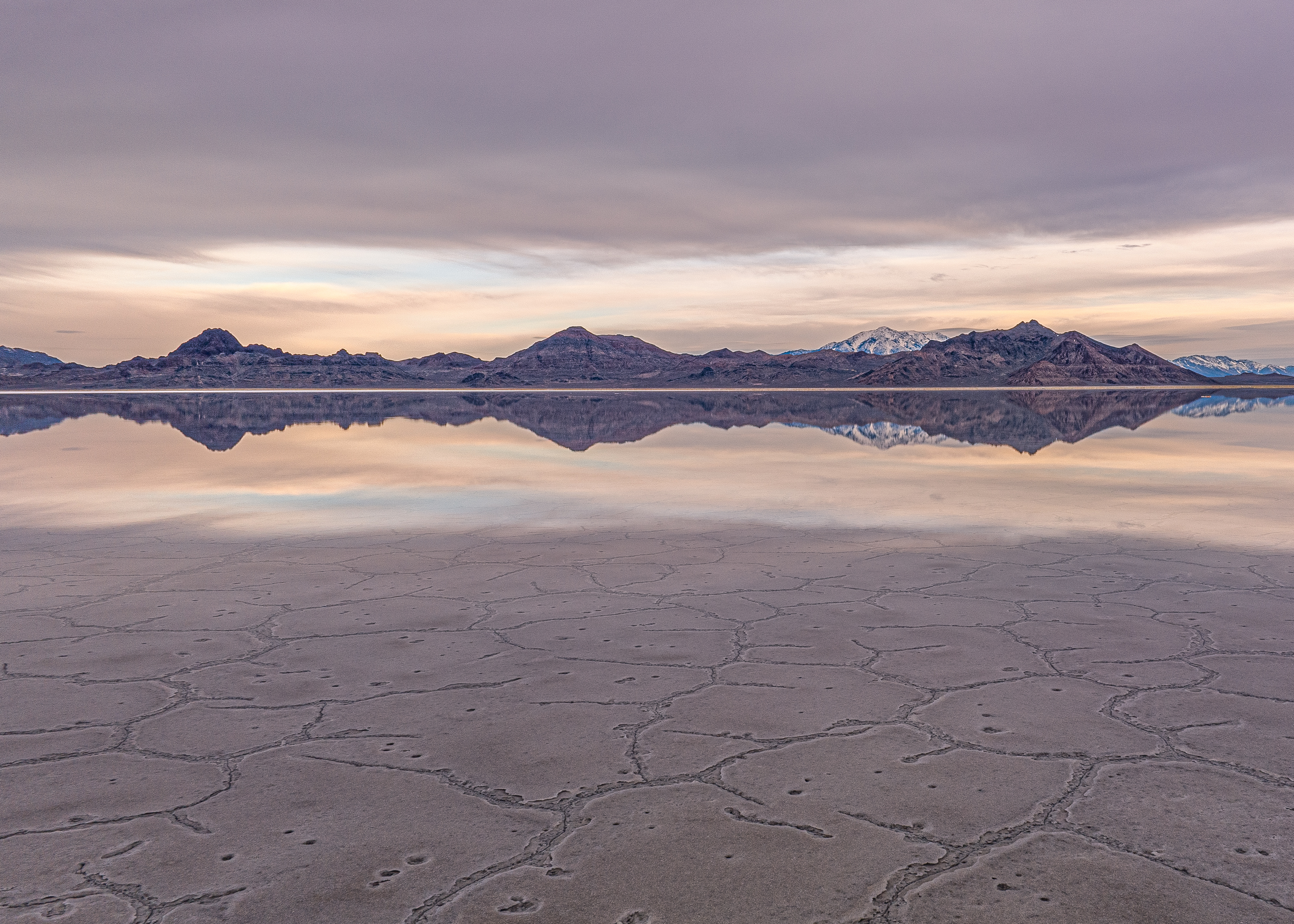 Salt flats with cracked patterns, reflecting mountain range and sky