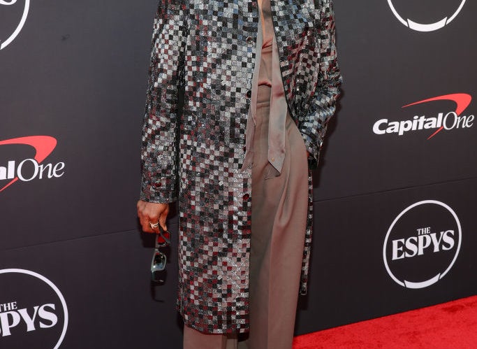 Colman Domingo on the red carpet at The ESPYS, wearing a checkered long coat over a grey pantsuit, holding sunglasses in his left hand
